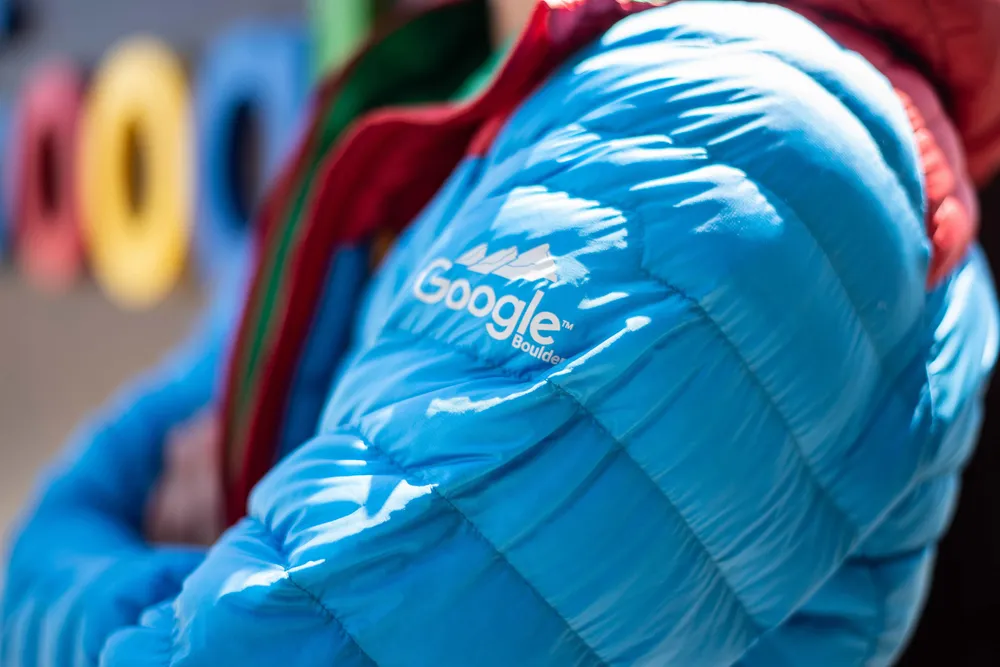 Custom made blue puff jacket with a white screen printed Google Boulder logo on the outside of the left arm