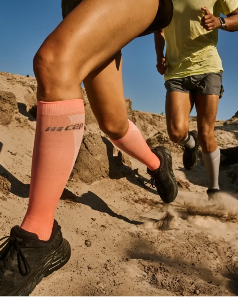Trail runner wearing ultra light compression socks on rocky trail with blue sky background