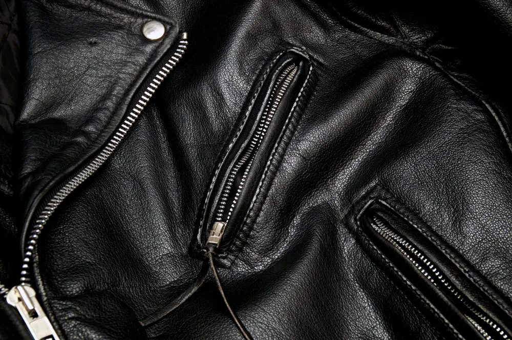 Detail of classic old black leather police style motorcycle jacket focusing on zippers and pockets.