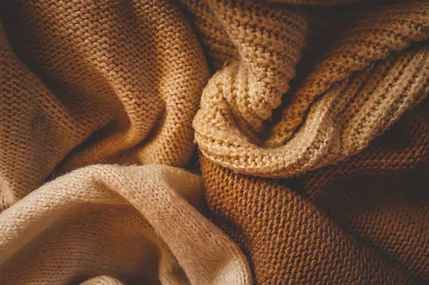 Close-up of soft, cozy, knitted beige and brown woolen blankets. Texture and folds of warm fabric creating a calm and relaxing autumn atmosphere.